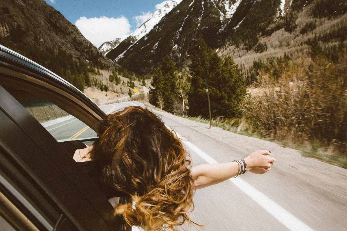 Une femme aux cheveux longs sort la main du véhicule sur route de montagne Une femme aux cheveux longs sort la main du véhicule sur route de montagne