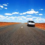 Une voiture blanche roule sur une route droite traversant un paysage aride